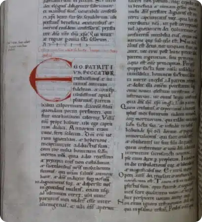 A page from an old manuscript with Latin text in black and red ink. The left column features a large red initial "E" with decorative lines, and handwritten notes about the History of St Patrick Ireland appear in the margins.